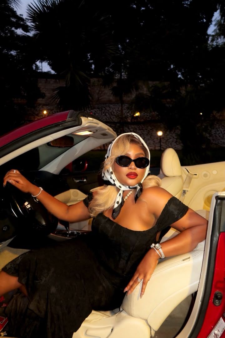 Woman in a black dress and headscarf posed in a red convertible at night